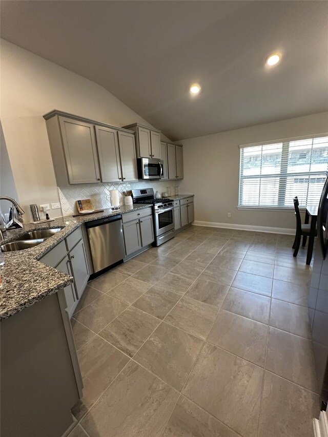 kitchen with stone counters, a sink, gray cabinetry, vaulted ceiling, and stainless steel appliances