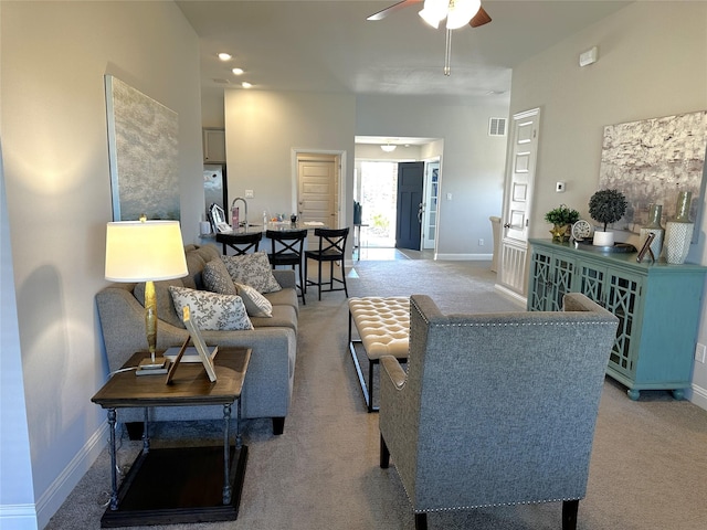 living room featuring visible vents, light colored carpet, baseboards, and a ceiling fan