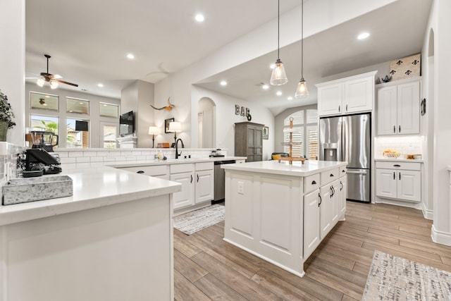 kitchen with tasteful backsplash, wood finish floors, ceiling fan, appliances with stainless steel finishes, and arched walkways