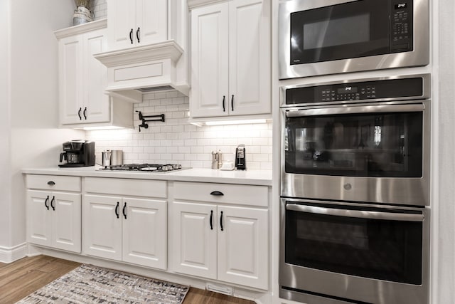 kitchen featuring wood finished floors, stainless steel appliances, white cabinets, light countertops, and decorative backsplash