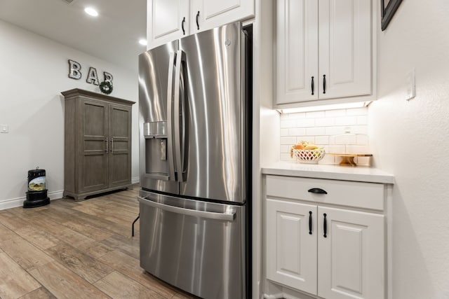 kitchen with wood finished floors, light countertops, white cabinets, stainless steel fridge, and tasteful backsplash