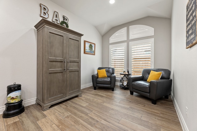 living area featuring vaulted ceiling, baseboards, and light wood finished floors