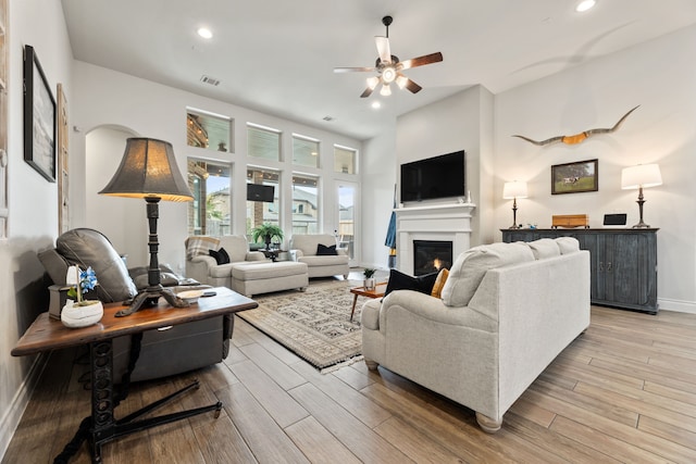 living room with visible vents, light wood-style flooring, a glass covered fireplace, baseboards, and ceiling fan