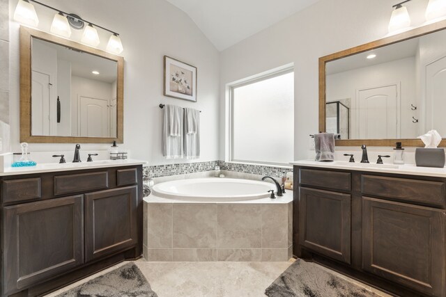 bathroom featuring two vanities, lofted ceiling, a bath, and a sink