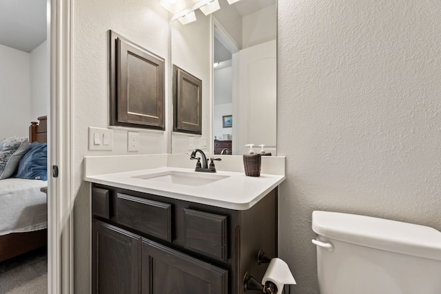 bathroom with connected bathroom, toilet, vanity, and a textured wall