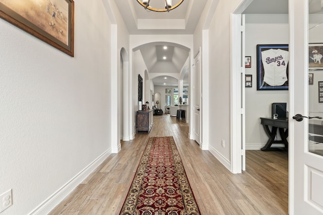 hall with light wood-type flooring, arched walkways, baseboards, and a chandelier