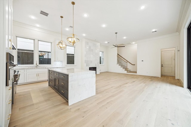 7527 Ciano Ln, Houston, TX 77055 - kitchen with ornamental molding, white cabinets, a center island, light wood-style flooring, and light stone countertops