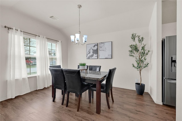 dining space featuring visible vents, a notable chandelier, wood finished floors, baseboards, and vaulted ceiling