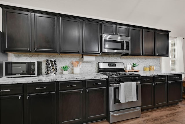 kitchen featuring light stone counters, decorative backsplash, appliances with stainless steel finishes, and wood finished floors