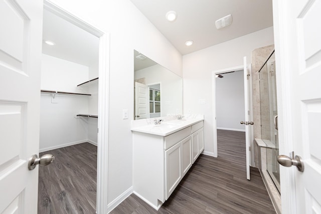 full bath featuring wood finished floors, vanity, a walk in closet, baseboards, and a stall shower