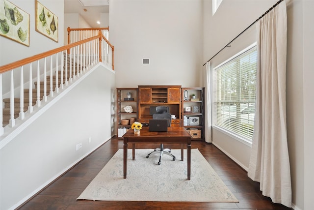 office with dark wood finished floors, visible vents, baseboards, and a towering ceiling