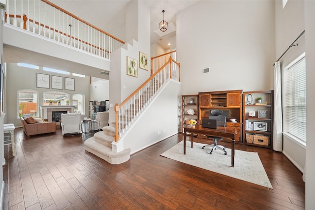 office area featuring visible vents, dark wood-style flooring, a towering ceiling, and baseboards