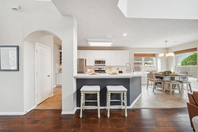 kitchen with a kitchen breakfast bar, white cabinetry, stainless steel appliances, light countertops, and dark wood-style flooring