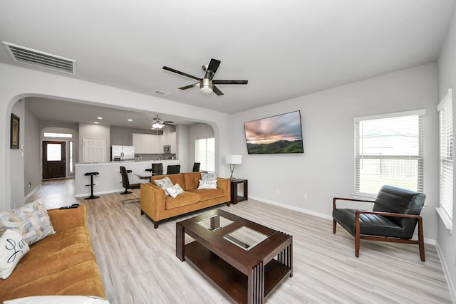 living room featuring arched walkways, visible vents, baseboards, and light wood-style floors