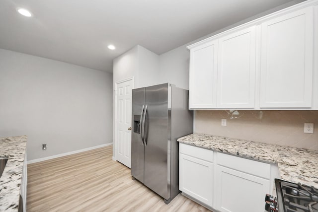 kitchen featuring light wood-style flooring, stainless steel appliances, white cabinets, decorative backsplash, and baseboards