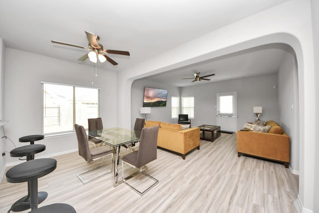 dining room featuring light wood-type flooring, arched walkways, baseboards, and ceiling fan