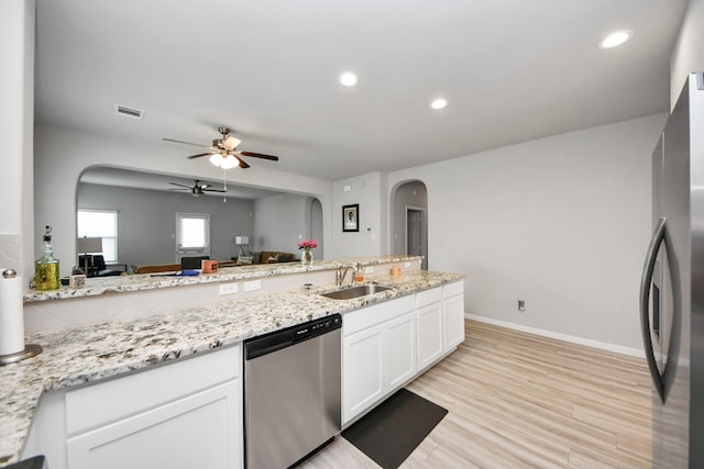 kitchen with a ceiling fan, a sink, white cabinetry, stainless steel appliances, and arched walkways