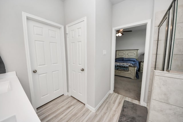 bathroom featuring wood finished floors, connected bathroom, baseboards, tiled shower, and vanity