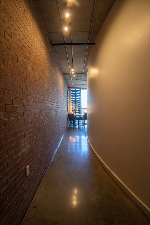 hallway with baseboards, concrete floors, and brick wall