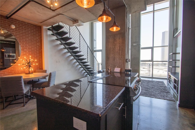 kitchen featuring finished concrete flooring, brick wall, range with electric stovetop, dark stone counters, and expansive windows