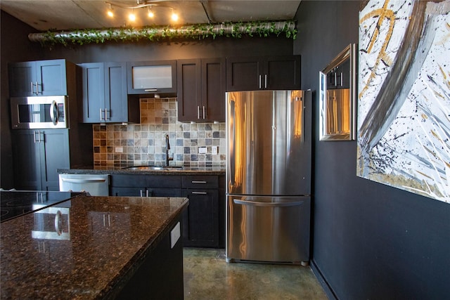 kitchen with finished concrete floors, dark stone counters, decorative backsplash, appliances with stainless steel finishes, and a sink