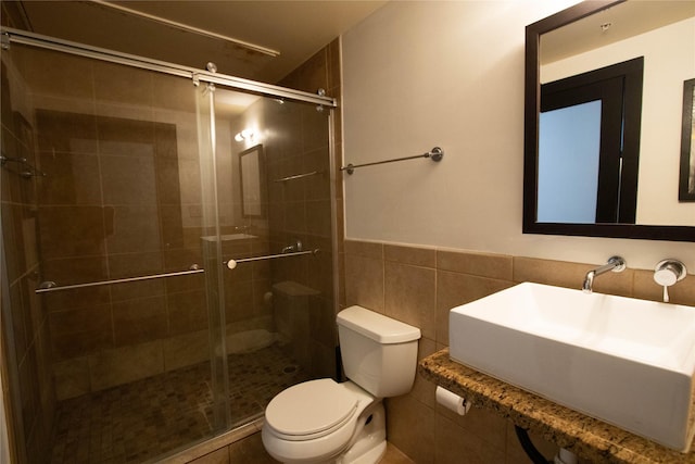 bathroom featuring a wainscoted wall, toilet, a stall shower, tile walls, and a sink