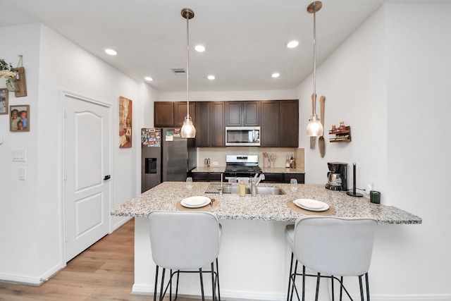 kitchen with light wood finished floors, dark brown cabinetry, a breakfast bar, a peninsula, and stainless steel appliances