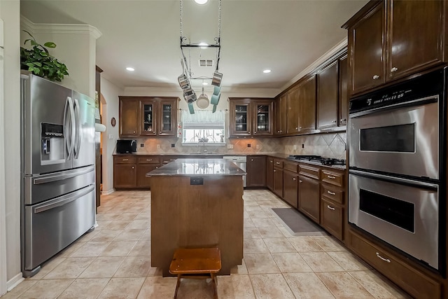 kitchen featuring light tile patterned floors, a sink, appliances with stainless steel finishes, tasteful backsplash, and a center island
