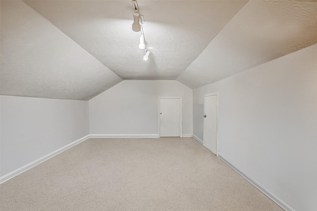 additional living space with baseboards, light carpet, a textured ceiling, and vaulted ceiling