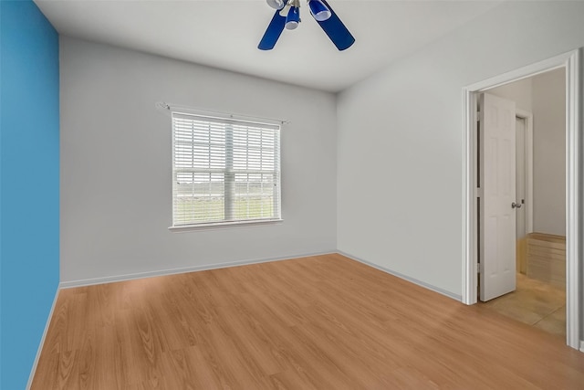spare room featuring a ceiling fan, baseboards, and light wood finished floors