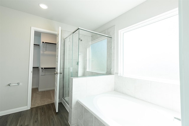 full bathroom featuring a shower stall, a spacious closet, a bath, and wood finished floors