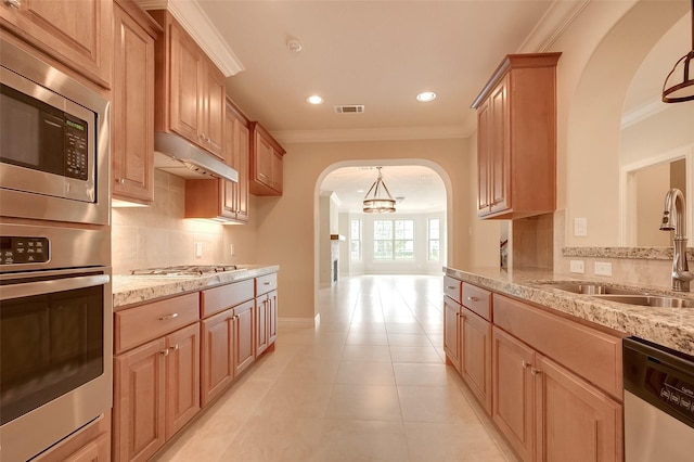 kitchen featuring crown molding, under cabinet range hood, appliances with stainless steel finishes, arched walkways, and a sink