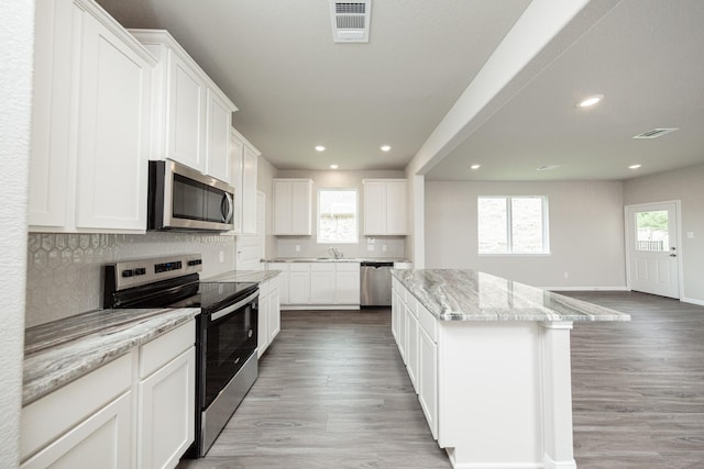 kitchen featuring light stone countertops, stainless steel appliances, light wood-type flooring, and a kitchen island