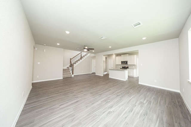 unfurnished living room featuring visible vents, baseboards, light wood-style flooring, and stairs