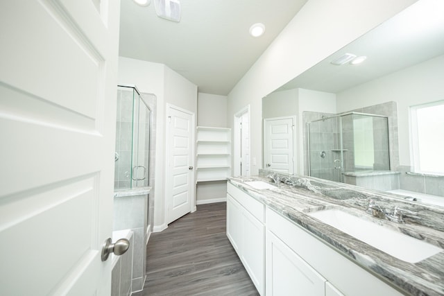 full bath featuring a shower stall, double vanity, a sink, and wood finished floors