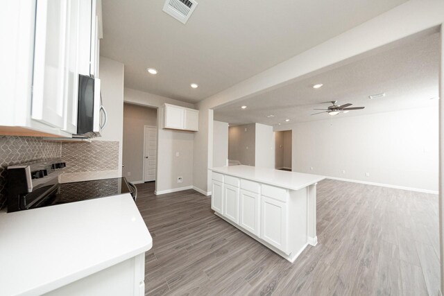 kitchen featuring backsplash, baseboards, white cabinets, light wood-style floors, and stainless steel microwave