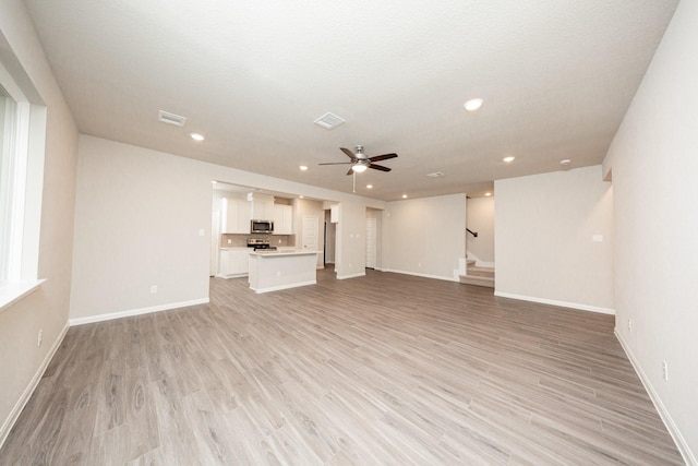 unfurnished living room featuring ceiling fan, stairs, light wood-style floors, baseboards, and recessed lighting