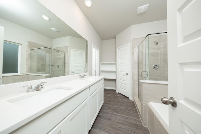 bathroom featuring a stall shower, double vanity, wood finished floors, and recessed lighting