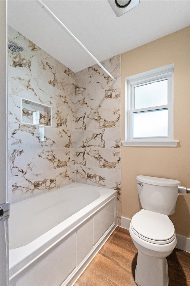 bathroom with baseboards, bathing tub / shower combination, wood finished floors, and toilet