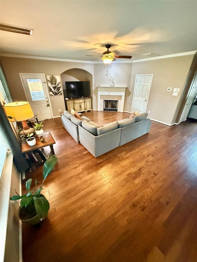 living area with wood finished floors, visible vents, ornamental molding, a fireplace, and ceiling fan
