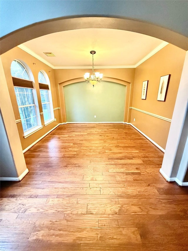 unfurnished dining area with arched walkways, a chandelier, wood finished floors, and ornamental molding