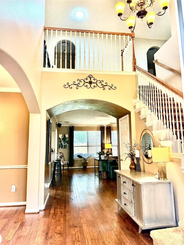 foyer with hardwood / wood-style floors, an inviting chandelier, baseboards, and arched walkways