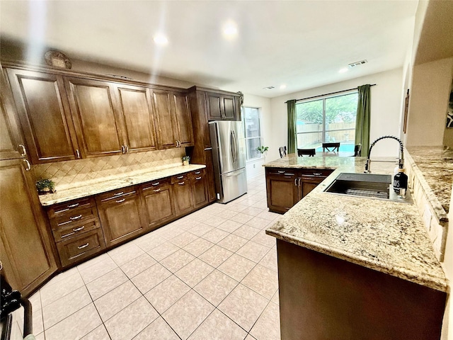 kitchen featuring a sink, light tile patterned flooring, freestanding refrigerator, backsplash, and light stone countertops