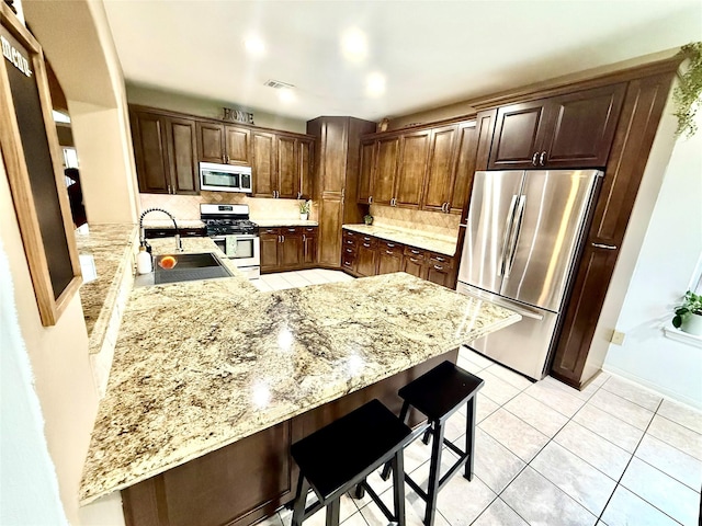 kitchen with stainless steel appliances, a peninsula, a kitchen breakfast bar, a sink, and decorative backsplash
