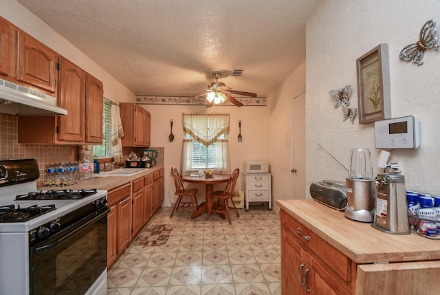 kitchen featuring white microwave, ceiling fan, under cabinet range hood, gas range, and a sink