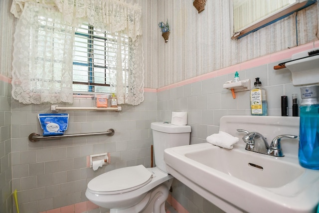 half bath featuring toilet, a sink, tile walls, wainscoting, and wallpapered walls