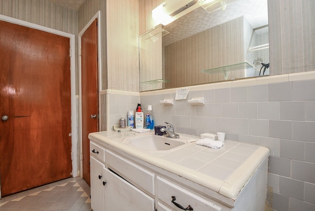 bathroom with tile patterned flooring, wallpapered walls, tile walls, a wainscoted wall, and vanity