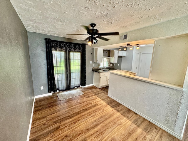 kitchen with wood finished floors, white cabinets, baseboards, ceiling fan, and a textured wall