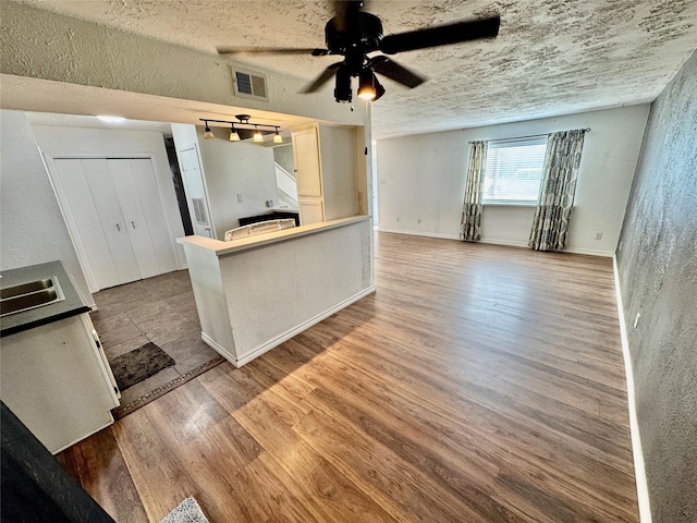 kitchen featuring visible vents, open floor plan, wood finished floors, a textured ceiling, and a ceiling fan