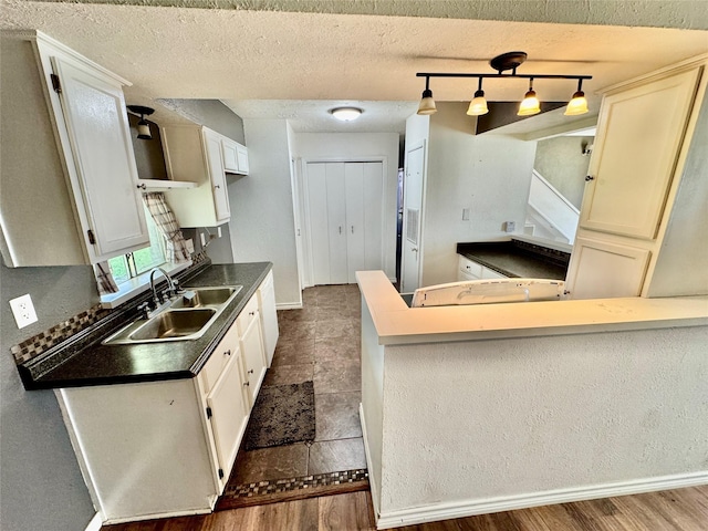 kitchen featuring dark countertops, baseboards, a peninsula, a textured ceiling, and a sink